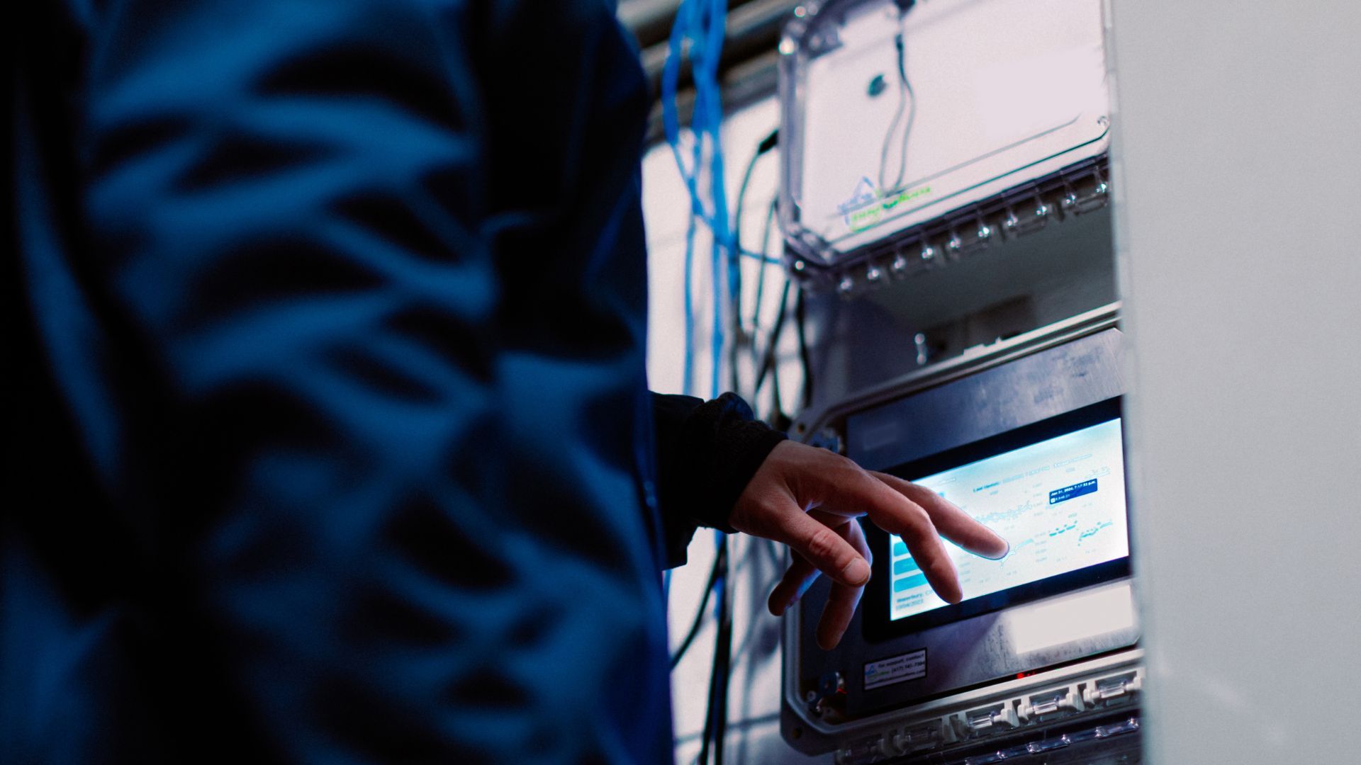 Factory worker in navy overalls touching a screen displaying manufacturing data
