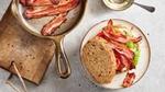 Top view of sandwich placed on a plate with a pan of bacon on the side.