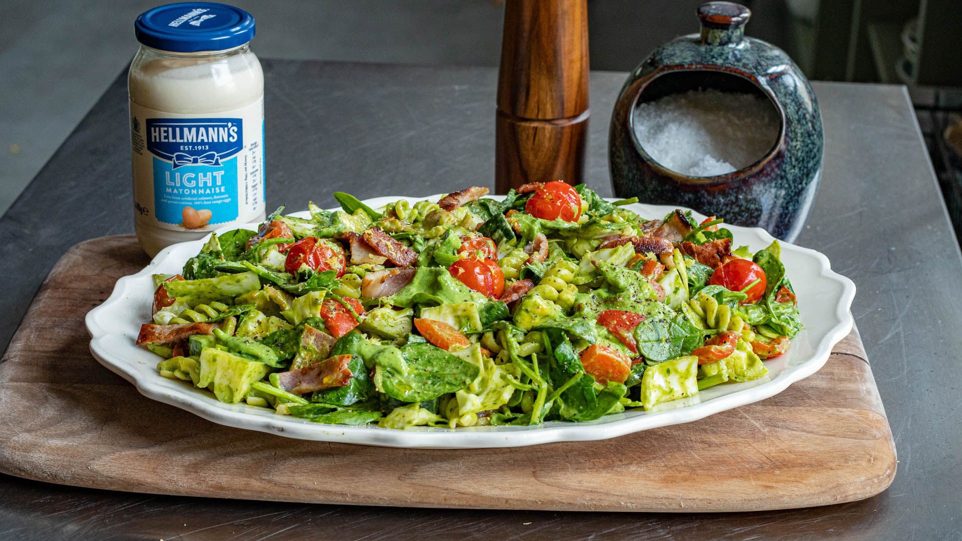 Jar of Hellmann’s Light Mayonnaise next to a plate of salad with a pepper mill and salt pot in the background.