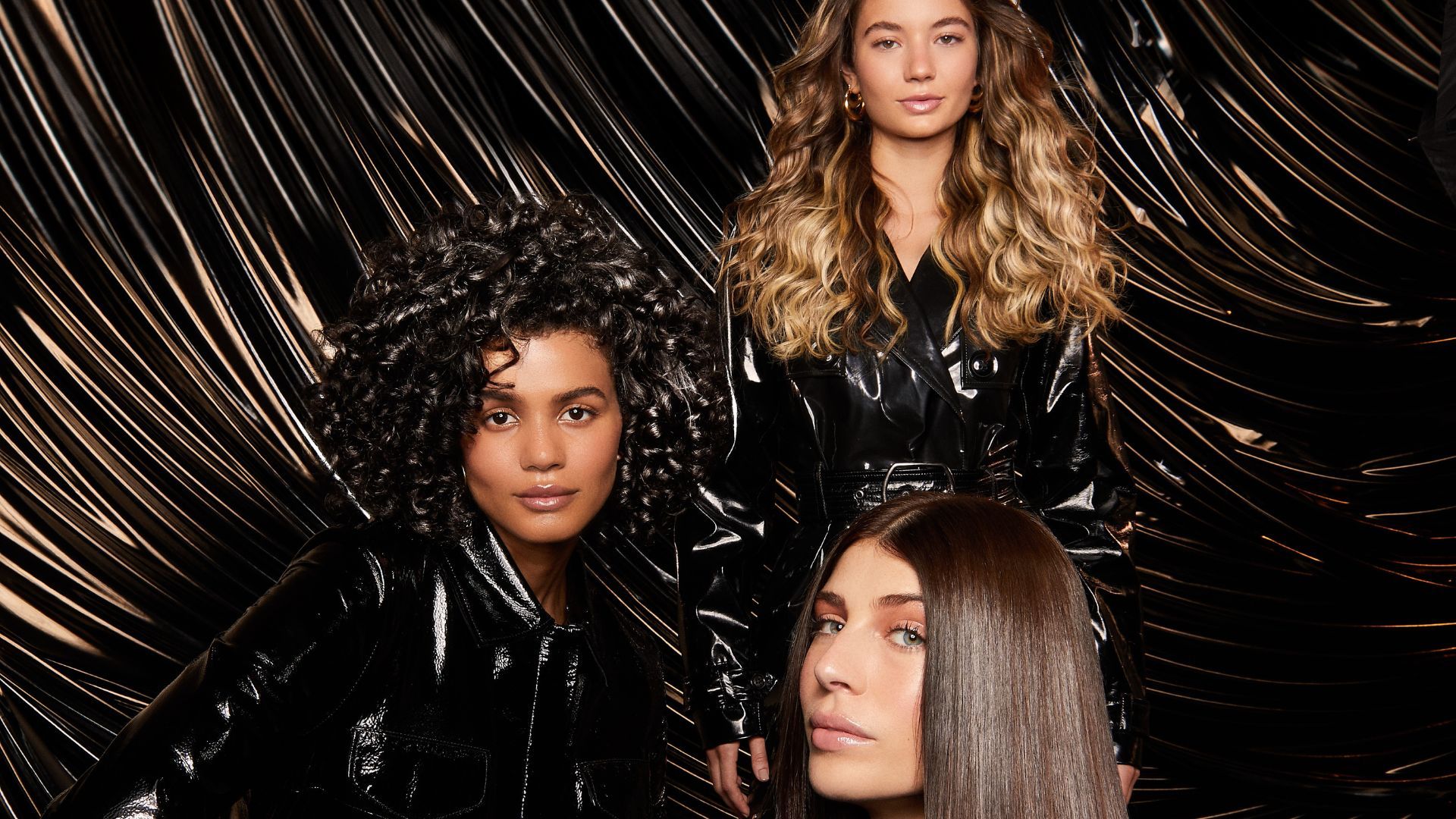 Three women with shiny hair, one blonde waves, one dark curls, one dark glossy hair. Pic is an ad for TRESemmé Lamellar Shine