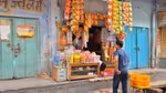 A man shops at a small store in rural India. Colourful goods are displayed on a table and hanging from the wall.
