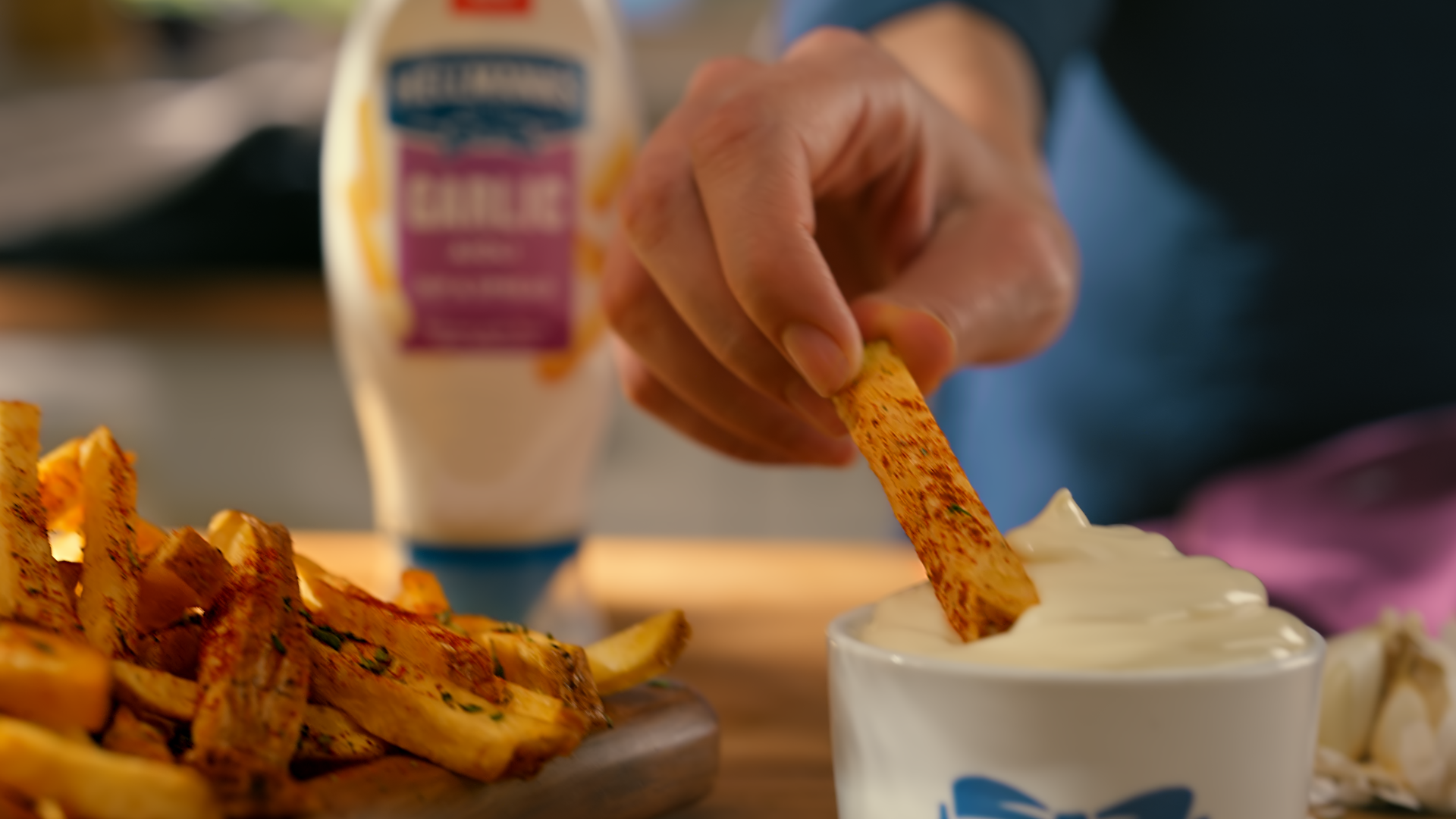 Close-up of a chip being tipped into a bowl of Hellmann’s flavoured garlic mayo.