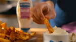 Close-up of a chip being tipped into a bowl of Hellmann’s flavoured garlic mayo.