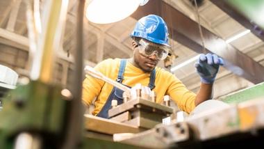 Man wearing hard hat and safety glasses working at a machine in a workshop