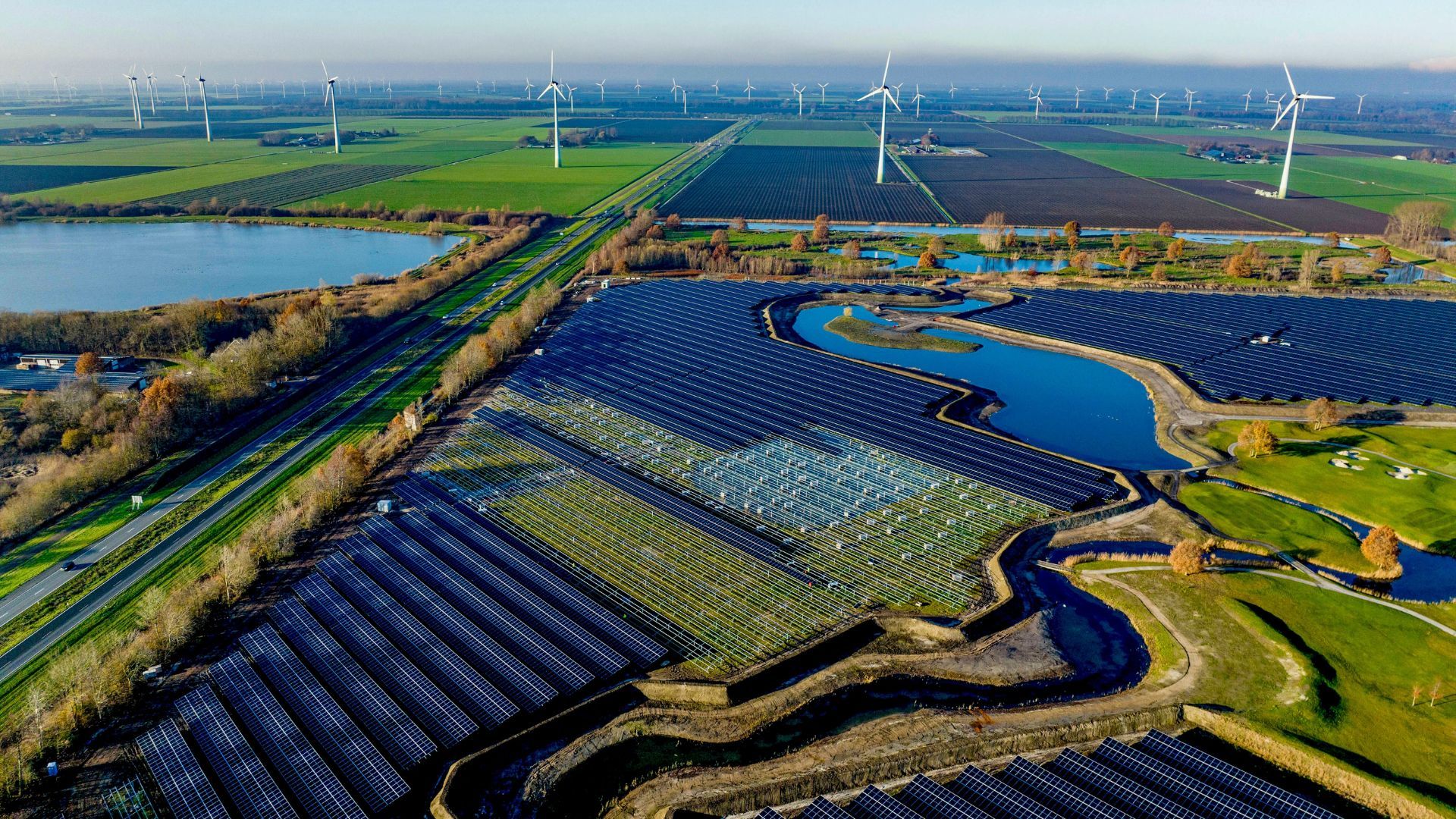 Aerial view of a vast solar panel farm followed by a wind farm among fields and lakes