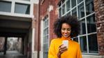 A woman in a city smiles as she looks down at her phone