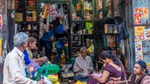 Three men and three women in saris sit outside a small store in rural India, surrounded by colourful products.