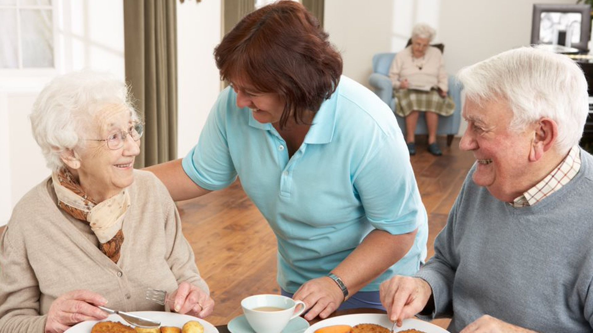 Two seniors being served a sandwich by a care assistant
