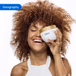 Person holding a Dove body care product in a bathroom setting with white tiles in the background.