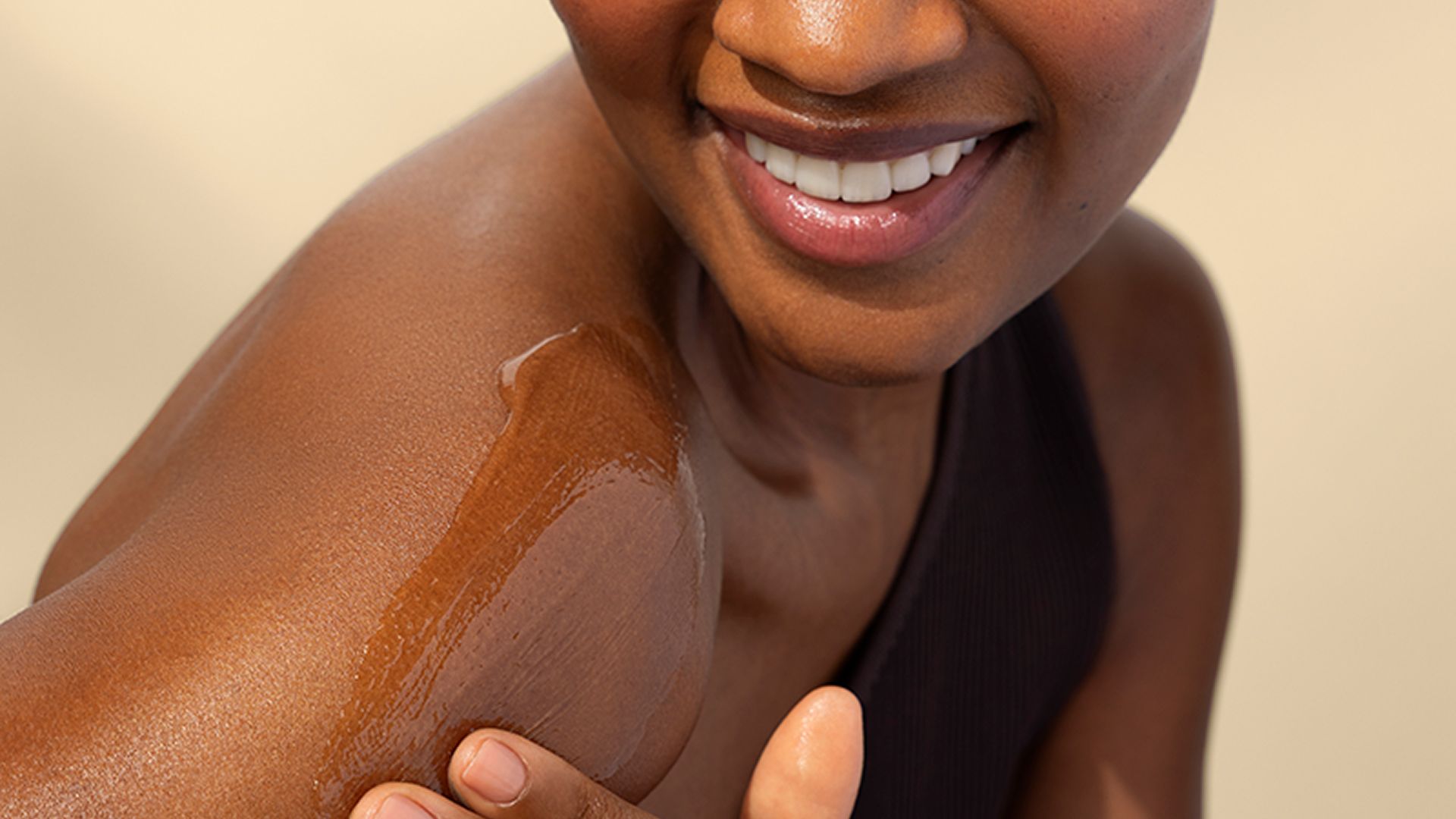 Close-up of a person applying a skincare product to their shoulder, showing smooth skin and a gentle smile.