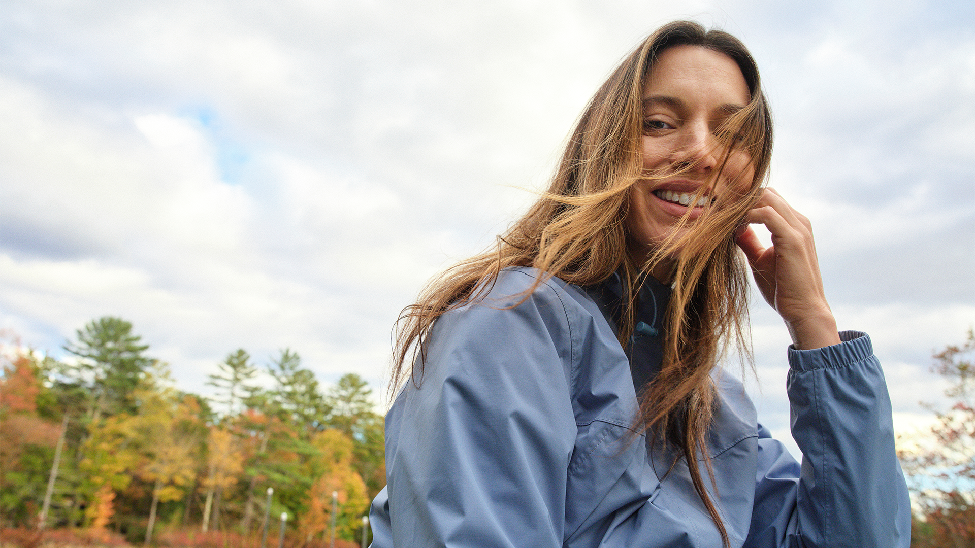 A girls sat outdoors wearing a blue windbreaker. The wind blows through her hair.