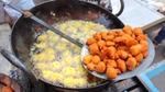 Street food fritters frying in a large pan of bubbling oil, with freshly cooked fritters resting on a slotted spoon.