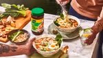 A table laid with two bowls of ramen noodles, a chopping board of ingredients and a jar of Knorr chicken bouillon.