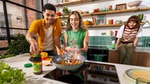 Two people in a kitchen are excited whilst stir-frying vegetables. On the counter is a open tub of Knorr Bouillon. In the background, there is a third person sat on the counter smiling.