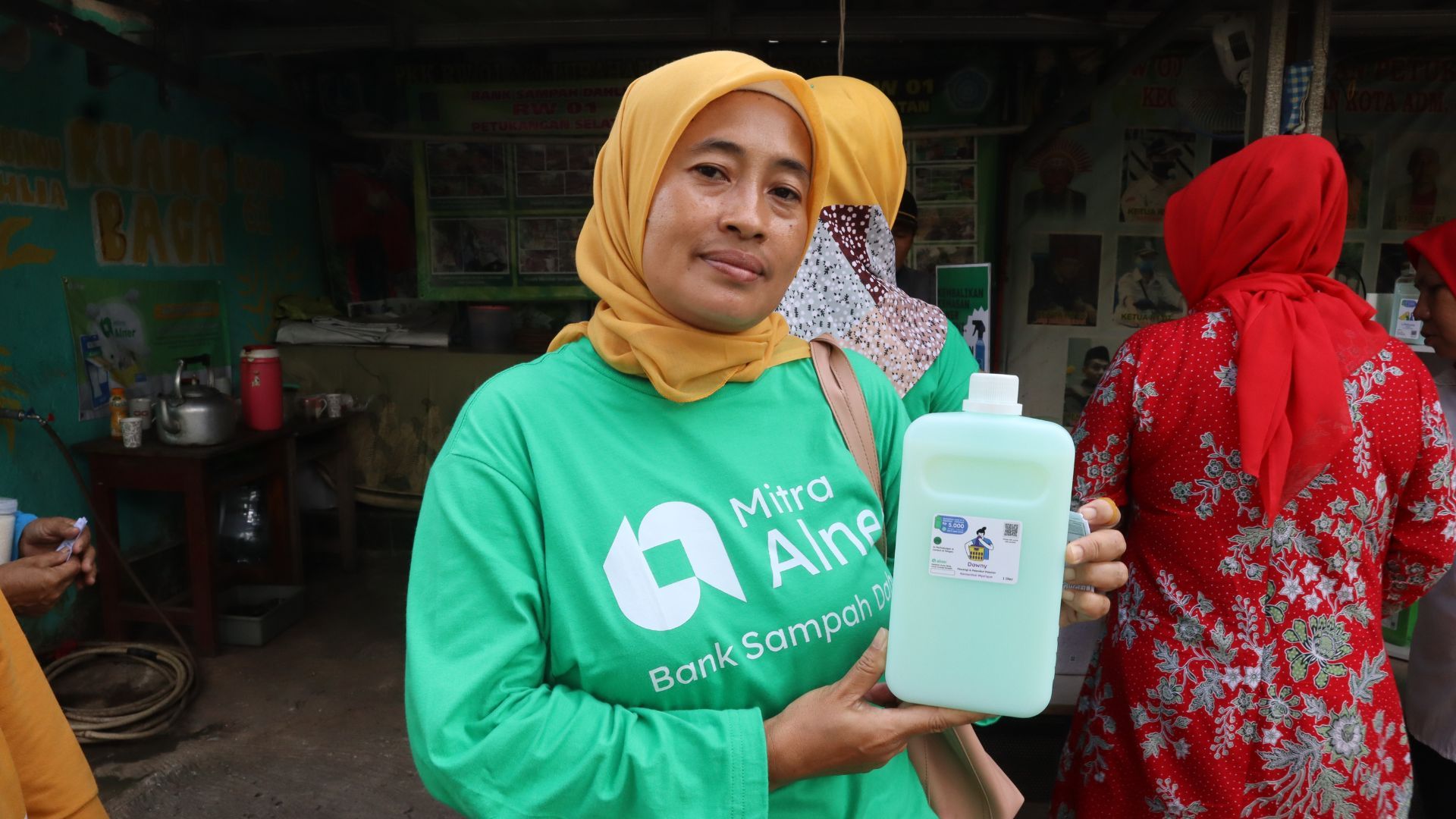 A women in a hijab and green shirt holding a bottle of product.