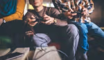 Photo focused in on the hands of three people sitting on a sofa using games consoles to play an online game